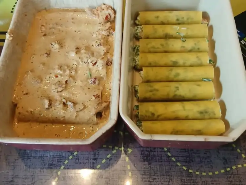Cannelloni ricotta e spinaci allineati in una pirofila, accanto a una seconda pirofila coperta di salsa alla panna con salmone e pomodori secchi