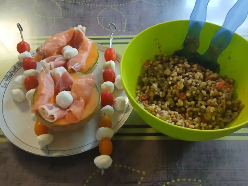 Mezzi meloni farciti di prosciutto crudo e bocconcini di mozzarella, spiedini di pomodorini e mozzarella, accanto a un’insalatiera
