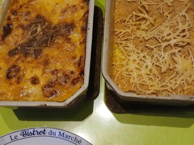 Porri gratinati dorati e purè fatto in casa gratinato al pangrattato, in due pirofile su un tavolo verde