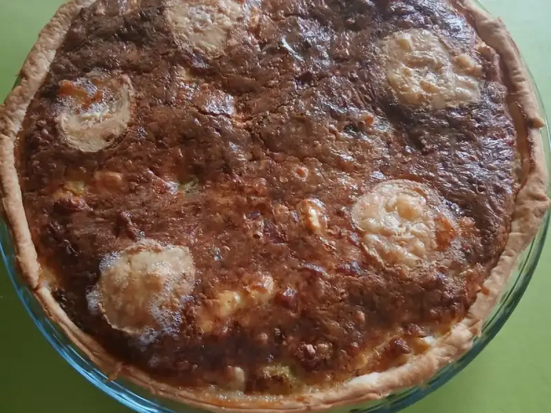 Quiche svuotafrigo ben dorata con rondelle di formaggio di capra, in uno stampo di vetro