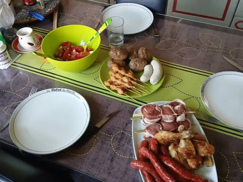 Spiedini di pollo crudi su una tavola da barbecue con salsicce, fusi di pollo, involtini con pancetta e insalata di pomodori